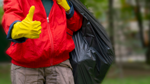 Persona tiene un sacco nero dei rifiuti mentre fa segno di OK con guanto giallo